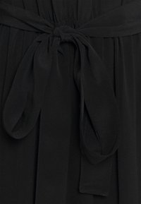 Schwarzes Kleid mit einem gerafften Bund und einem Stoffbindeband. Glattes, leichtes Material mit matter Oberfläche; keine sichtbaren Muster oder Beschläge.