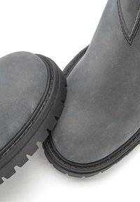 Gray suede ankle boots with a rounded toe, textured surface, and a rugged black rubber sole featuring a pronounced tread pattern.