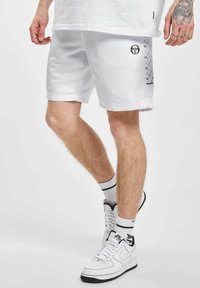 Hvite sports shortser laget av lett materiale, med svart logo og mønstret sidelomme. Kombinert med høye hvite joggesko.