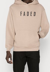Felpa beige con una grande stampa nera "FADED" sul fronte, dotata di tasca a marsupio e polsini a coste. Realizzata in tessuto morbido.
