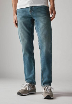 Lichtblauwe denim jeans, rechte pasvorm, met subtiele vervaging en tonale stiksels, gecombineerd met grijze en witte sportschoenen.