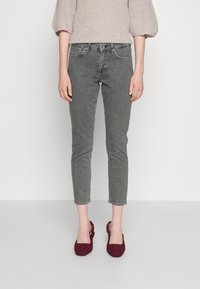 Jean skinny en denim gris avec un design ajusté. Présente un style traditionnel à cinq poches et une légère coupe au niveau de la cheville. Associé à des ballerines tissées bordeaux.