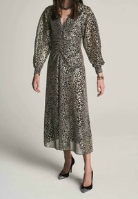 Robe longue noire et argentée avec un motif, dotée de manches bouffantes et d'une taille cintrée. Tissu transparent avec une jupe fluide, associée à des talons noirs.