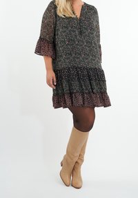 Vestido negro floral con dobladillo de volantes y mangas acampanadas, que presenta pequeños patrones en rosa y verde. Combinado con botas beige hasta la rodilla.