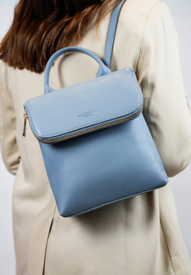 Lichtblauwe leren rugzak met een ritssluiting, platte voorklep en handvat aan de bovenkant. Voorzien van een schouderriem en een gestructureerde afwerking.