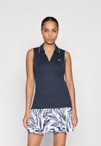 Top polo azul-marinho sem mangas com textura canelada e colarinho branco; combinado com uma saia branca com padrão abstrato azul e design evasê.