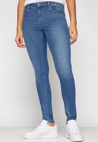 Blå denim skinny jeans med hög midja, femficksdesign och lätt stretch. Kombinerat med vita sportiga sneakers för kontrast.