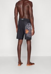 Bañador negro con un diseño gráfico que presenta detalles intrincados y colores, incluyendo llamas y patrones circulares en la parte trasera.