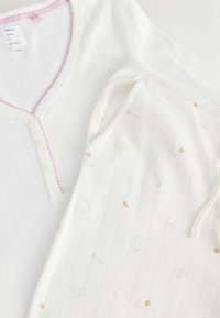 Ensemble de pyjama blanc en maille côtelée comprenant un haut à col en V boutonné bordé de rose et un pantalon assorti à cordon de serrage avec un petit imprimé floral.