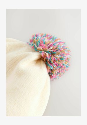 Pletená krémová čiapka s mnohofarebným pompónom na vrchu. Pompón obsahuje ružové, modré a hnedé vlákna, čím pridáva textúru a farebný kontrast.