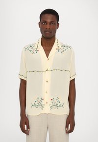 Camisa amarilla de manga corta con bordados florales en verde, rojo y amarillo. Presenta una parte frontal con botones y un dobladillo redondeado. Tejido ligero.