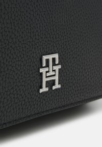 Schwarze strukturierte Lederhandtasche mit einem silbernen Logoakzent. Die Oberfläche hat ein genarbtes Finish, das dem Material Tiefe und Details verleiht.