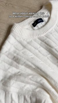Pull blanc en maille torsadée avec col rond côtelé posé sur une surface en bois, le texte demande s'il convient pour un rendez-vous café décontracté en hiver.