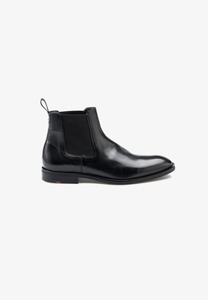 Black leather Chelsea boot with elastic side panels, a pull tab at the back, and a slim rubber sole. Smooth finish and pointed toe design.