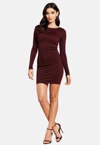 Burgundowa, prążkowana sukienka z długim rękawem o dopasowanym kroju, długości powyżej kolan i miękkiej teksturze. Dobrana z czarnymi, sandałami na wysokim obcasie.
