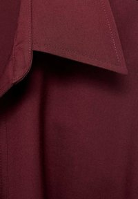 Bordo majica s oštrim ovratnikom. Glatka tekstura i precizni detalji šivenja, koji prikazuju krojeni dizajn.