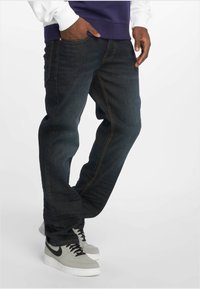 Mørkeblå denimjeans med rett passform, med gule sømdetaljer. Kombinert med grå Nike Air Force 1-sneakers.
