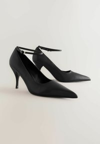 Mustat nahkakengät, joissa on korkeat korot, terävä kärki, nilkkahihna ja hoikka stiletto-korko, joissa on sileä pinta ja minimalistinen muotoilu.