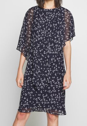 Granatowa sukienka do kolan z białym kwiatowym wzorem, przezroczystymi falbanowymi rękawami i luźnym szalowym detalem opadającym z przodu.