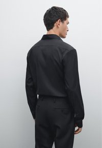 Black long-sleeve shirt with a pointed collar and buttoned cuffs, paired with matching tailored pants in a smooth fabric.