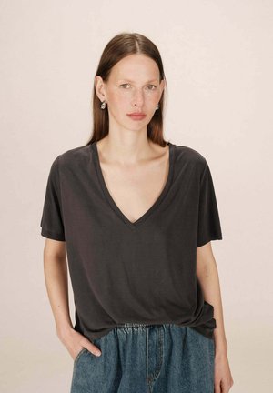 T-shirt en coton gris avec un décolleté en V, coupe décontractée et manches courtes. Porté avec un short en denim avec une taille élastique et des poches.