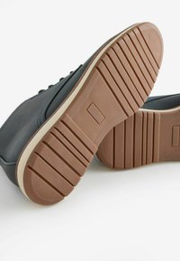 Zapatillas de piel azul oscuro con una suela de goma de color claro que presenta un patrón de banda de rodadura texturizada. Con detalles de cordones a juego.