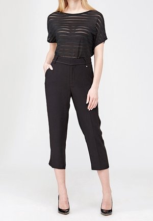 Czarna, w paski, luźna bluzka połączona z dopasowanymi, czarnymi, krótkimi spodniami. Materiał wydaje się lekki o gładkiej fakturze. Całość uzupełniają czarne szpilki.