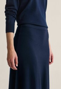 Merisotilaansininen neulepaita ja hame -setti. Sileä pinta, istuva neulepaita resorireunuksilla ja laskeutuva hame, jossa on hienovarainen kiilto.