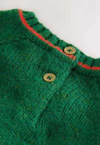 Vêtement tricoté vert avec une surface texturée, orné d'un accent rouge le long du col et de deux boutons marron clair.