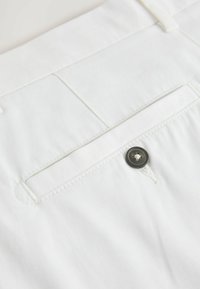 Tissu blanc comprenant une poche arrière avec un bouton noir et des détails de coutures, mettant en valeur une texture lisse et un design épuré.