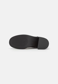 Semelle de chaussure noire au design plat, en caoutchouc texturé pour une meilleure adhérence, avec un bord lisse. Style minimaliste sans logos ni motifs visibles.