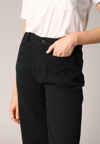 Zwarte broek met een hoge taille, gemaakt van stevige stof, voorzien van twee voorzakken en een enkele knoopsluiting. Gecombineerd met een lichte t-shirt.