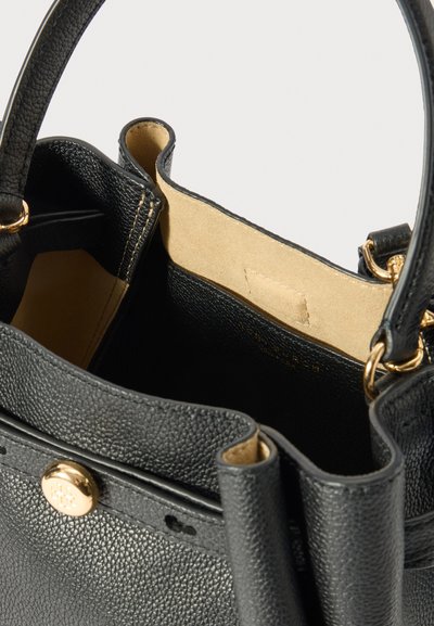 Črna torbica iz pebble usnja z zlatim gumbom za zapiranje, bež suknjena notranja obloga in črni usnjeni ročaji z zlatimi zaključki.