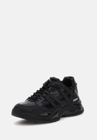 Sneaker sportivo nero con tomaia sintetica lucida, accenti testurizzati, suola spessa e dettagli del logo ben visibili sul lato.