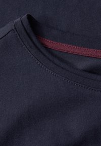 Camiseta de algodón azul marino con escote redondo que presenta un acento texturizado rojo en el interior del cuello y detalles de costura visibles.