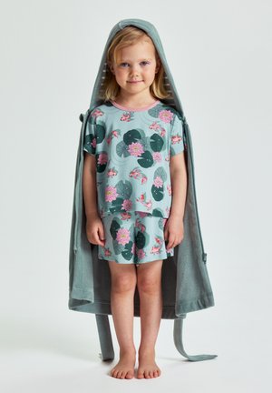 Jong meisje dat blootsvoets staat, gekleed in een bijpassende blauwe pyjama met koi-karpers en waterlelies, gewikkeld in een badjas met capuchon.