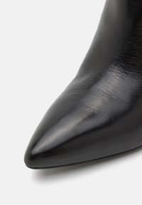 Bottine en cuir noir avec un bout pointu et une texture lisse. La surface apparaît brillante et présente un design épuré.