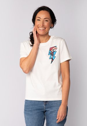 T-shirt en coton blanc avec un graphique coloré d'un patin à roulettes à l'intérieur d'un éclair sur le côté gauche de la poitrine. Manches courtes, coupe décontractée.