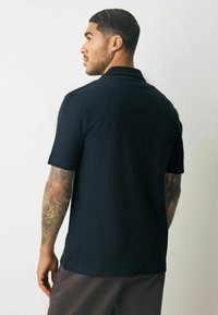 Korte mouwen marineblauwe polo shirt van gestructureerde stof, met een klassieke kraag en een rechte zoom, gedragen met donkere broek.