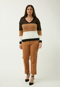 V-hals striktrøje i sort, brun og hvid; ribbet tekstur. Lysebrune bukser med manchetter, parret med sorte spidse hæle.