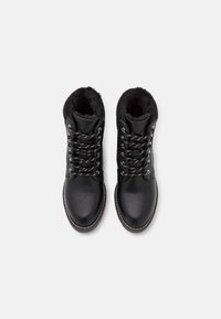 Botas de cuero negro con forro de piel sintética, que presentan ojales metálicos plateados, cordones negros y punta redondeada. Suela de goma con detalles cosidos.