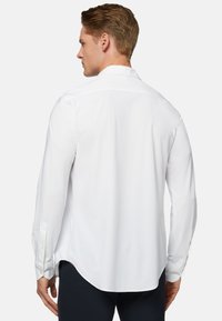 Chemise blanche à manches longues en tissu lisse, dotée d'un col standard, de poignets à boutons et d'un ourlet arrondi à l'arrière.