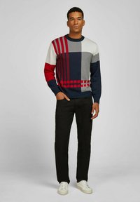 Strickpullover mit einem Farbblockdesign in Marineblau, Grau, Rot und Weiß, mit verschiedenen Mustern. Schwarze Hose und weiße Sneakers runden den Look ab.