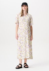 Robe midi florale en crème avec des motifs jaunes et violets, manches courtes à volants, décolleté en V et coupe décontractée. Portée avec des sandales noires.