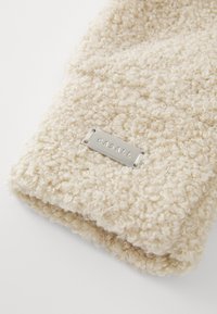 Beige textured fabric with a looped design and a silver Casall logo tag attached, showcasing soft and plush material.
