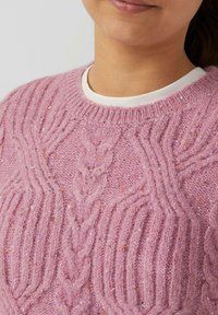 Rosa gestrickter Pullover mit strukturierten Kabelmustern und subtilen Sprenkeln. Mit rundem Halsausschnitt und gerippten Bündchen. Weiches, kuscheliges Material.