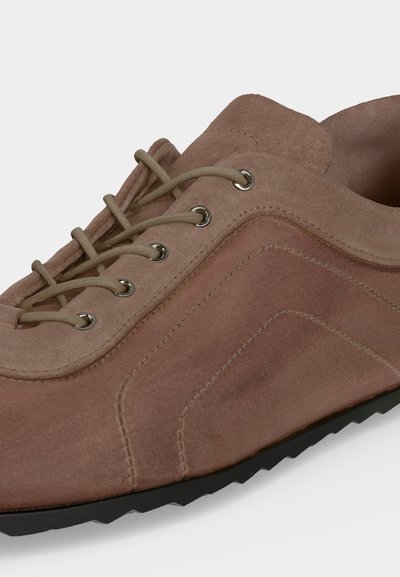 Gros plan d'une chaussure décontractée en daim marron avec des lacets assortis, des œillets en métal et une semelle en caoutchouc noire.