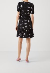 Svart blommig klänning med korta puffärmar och en volangkant, med lila och vita blommönster. Bärs med rosa klacksandaler.