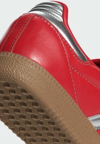 Röda lädersneakers med silverdetaljer, texturerad brun gummisula och detaljerad sömnad. Har en rund tå och låg profil.