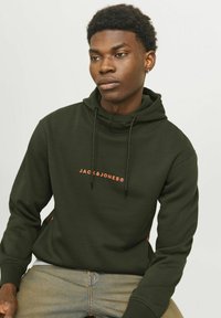 Mørkegrøn hoodie med høj krave, justerbare snører og et logo i orange på brystet. Lavet af bomuldsstof, afslappet pasform.